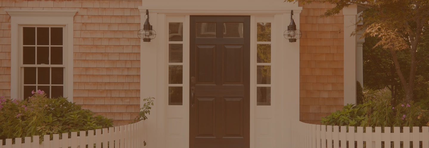 Front of a house with cedar shake siding and black front door with white picket fence