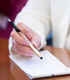 Image of a woman's hand holding a pen near a notepad on desk