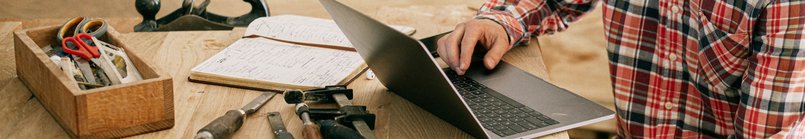 Cropped photo of man wearing flannel shirt using a laptop with woodworking tools on table