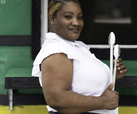 A woman small business owner standing in front of her food truck, holding cooking tongs