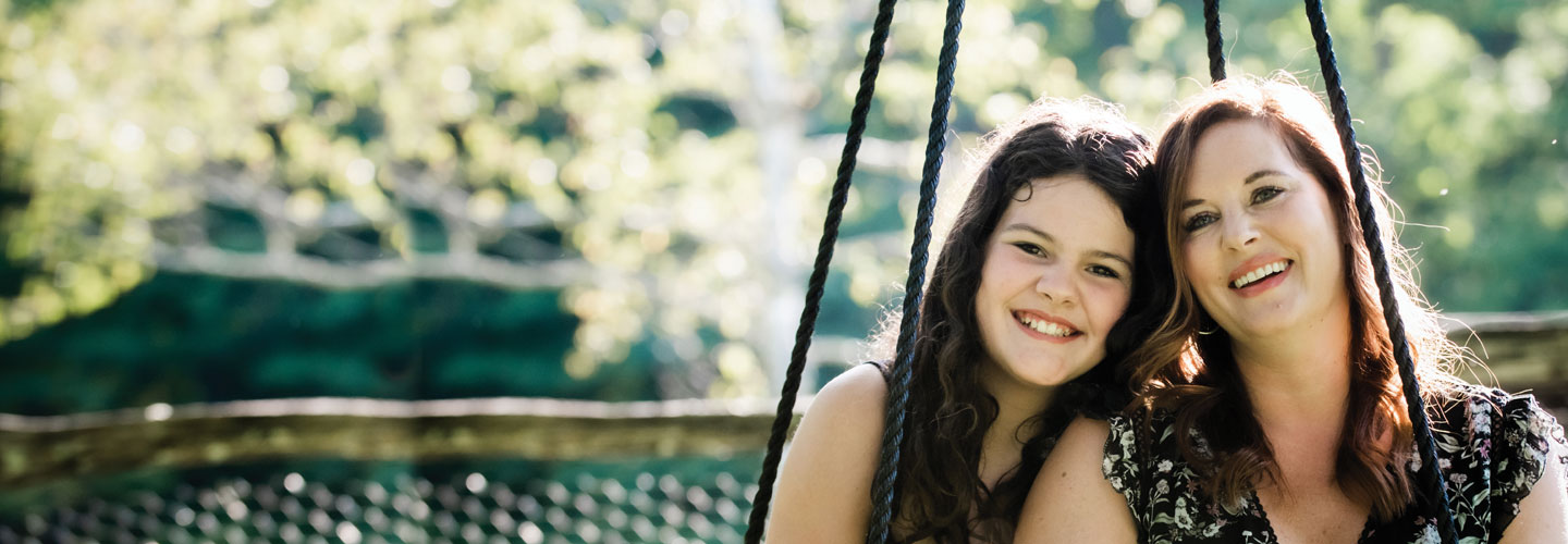 Photo of smiling mother and daughter outside with green background behind them