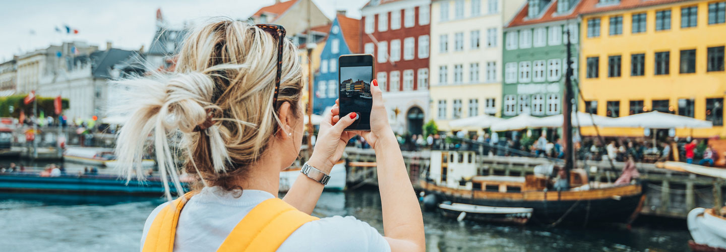 Woman holding her phone and taking a photo on vacation in a beautiful European waterfront destination