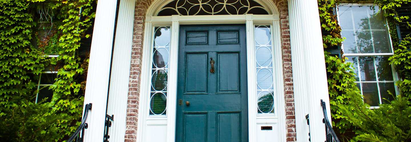 photo of blue-green colored front door with white columns and brick facade covered by ivy