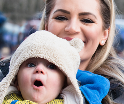 Cropped photo of young woman holding surprised baby wearing winter hat